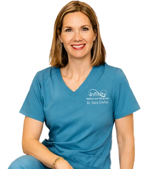 Studio portrait of a Dr. Sara Stefan wearing blue scrubs, seated against a transparent background.